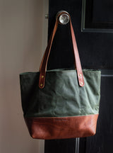 A green canvas and brown leather tote bag hangs from a doorknob.
