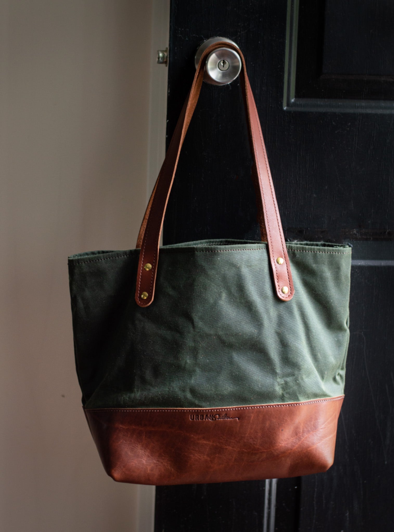 A green canvas and brown leather tote bag hangs from a doorknob.
