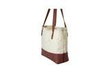 A cream canvas tote bag with brown leather base and handles sits upright.
