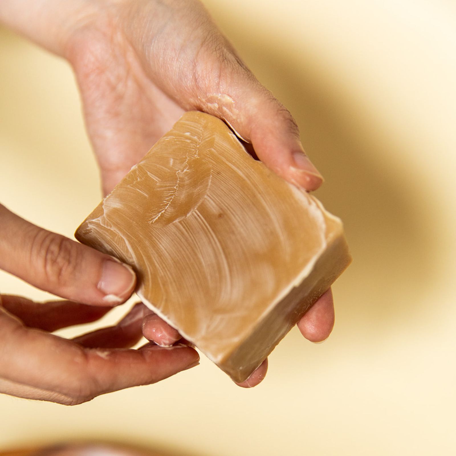 Hand holding a bar of soap against a blurred yellow background