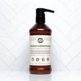 A bottle of Rustic Strength coconut conditioner with lavender and tea tree oil sits on a white marble surface.