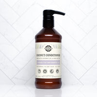 A bottle of Rustic Strength coconut conditioner with lavender and tea tree oil sits on a white marble surface.