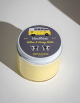 A jar of VanMan's Tallow & Honey Balm displays a retro VW bus and cows on its label, advertising its natural ingredients.
