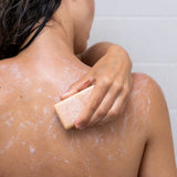 Woman scrubs her back with a moisturizing natural soap bar in the shower.
