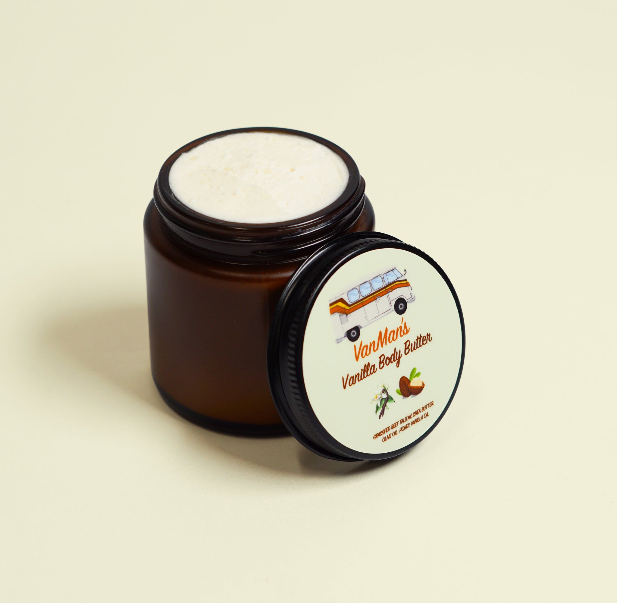 An open jar of VanMan's Vanilla Body Butter displays its creamy texture with the lid featuring a vintage bus design.
