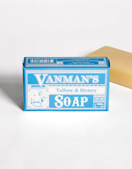 A bar of Vanman's Tallow & Honey Soap sits in its blue packaging next to a single unwrapped bar.
