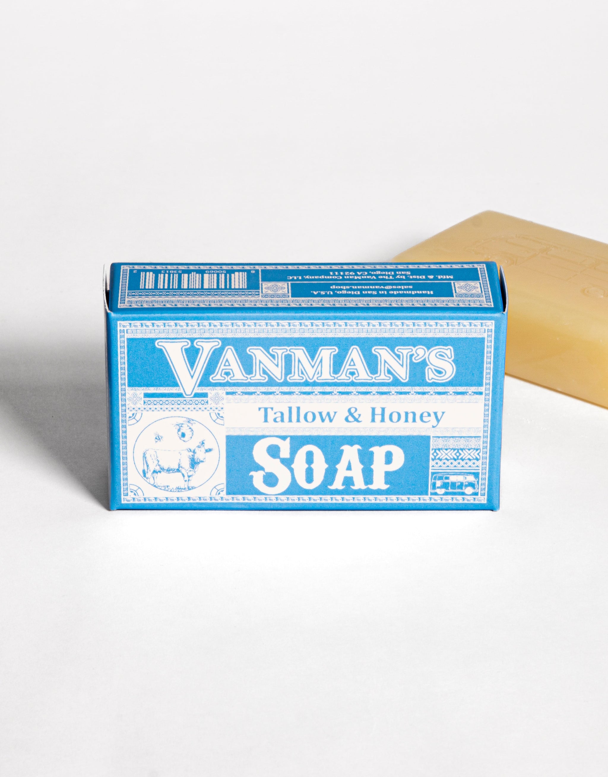 A bar of Vanman's Tallow & Honey Soap sits in its blue packaging next to a single unwrapped bar.
