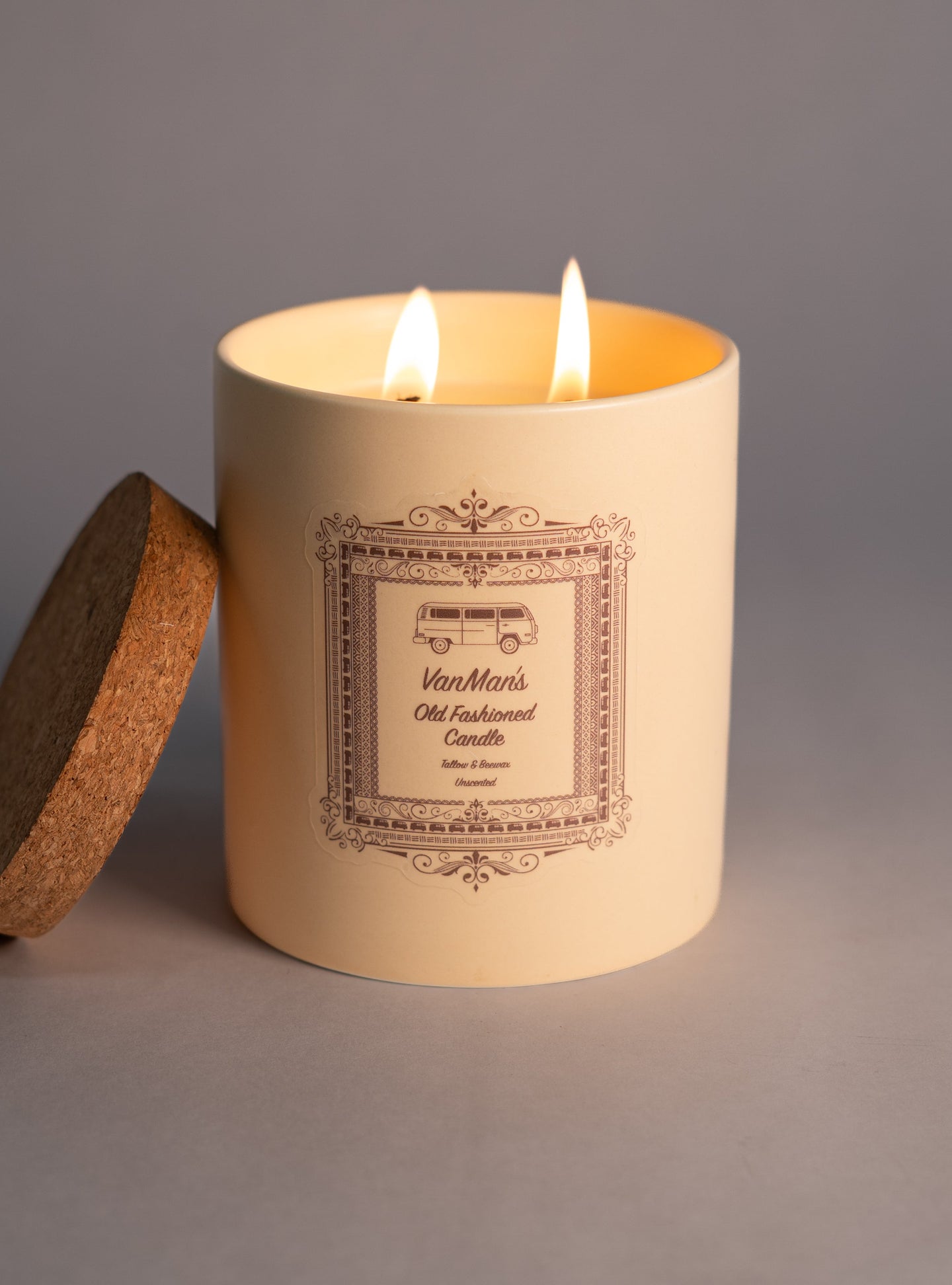 Two flames burn atop a VanMan's Old Fashioned tallow and beeswax candle with a cork lid resting beside it.
