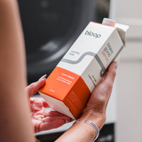 A woman holds a carton of Bloop Super Bloom laundry soap, highlighting its eco-friendly, sustainable packaging.
