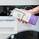 Woman pours eco-friendly "Make good sense" laundry detergent from a carton into a washing machine dispenser.