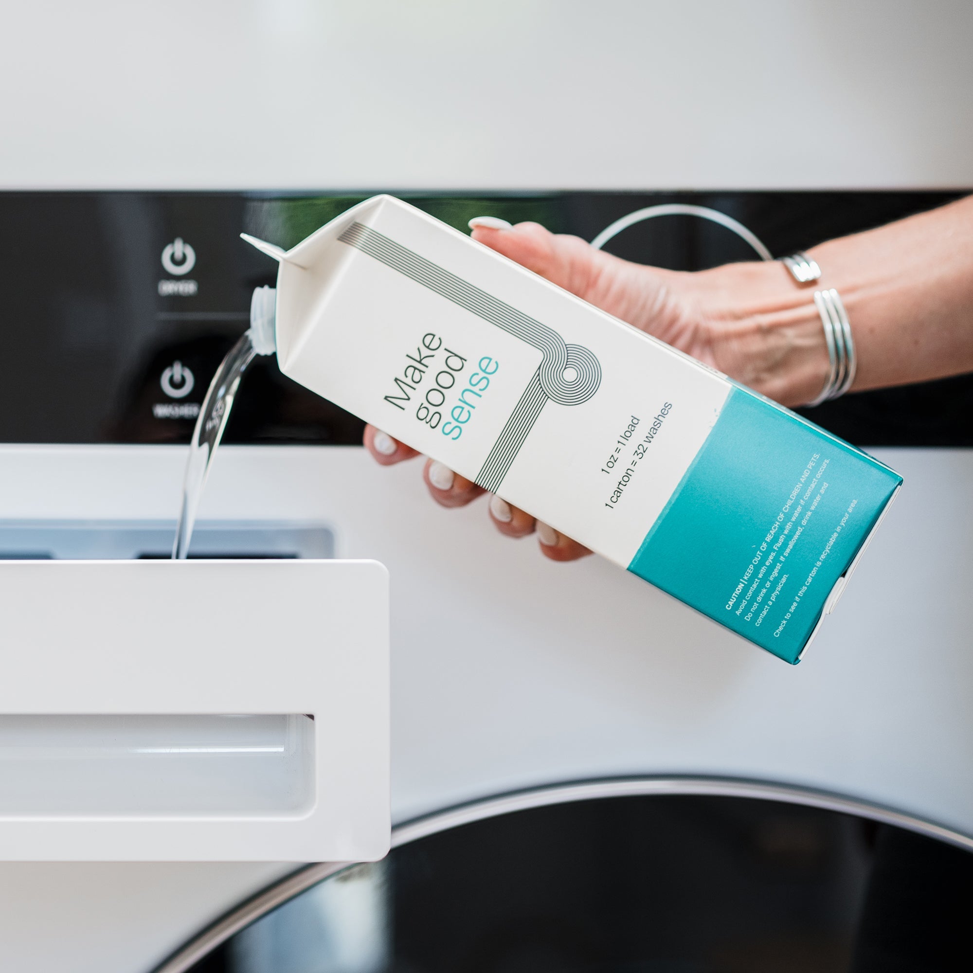 Woman pours liquid laundry detergent from a "Make good sense" carton into a washing machine dispenser.
