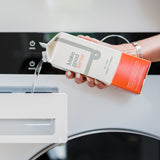 A person pours eco-friendly "Make Good Sense" laundry detergent from a carton into a washing machine dispenser.
