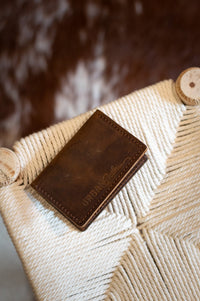 Rustic leather wallet displaying "Urban Southern" sits on a woven rope chair.
