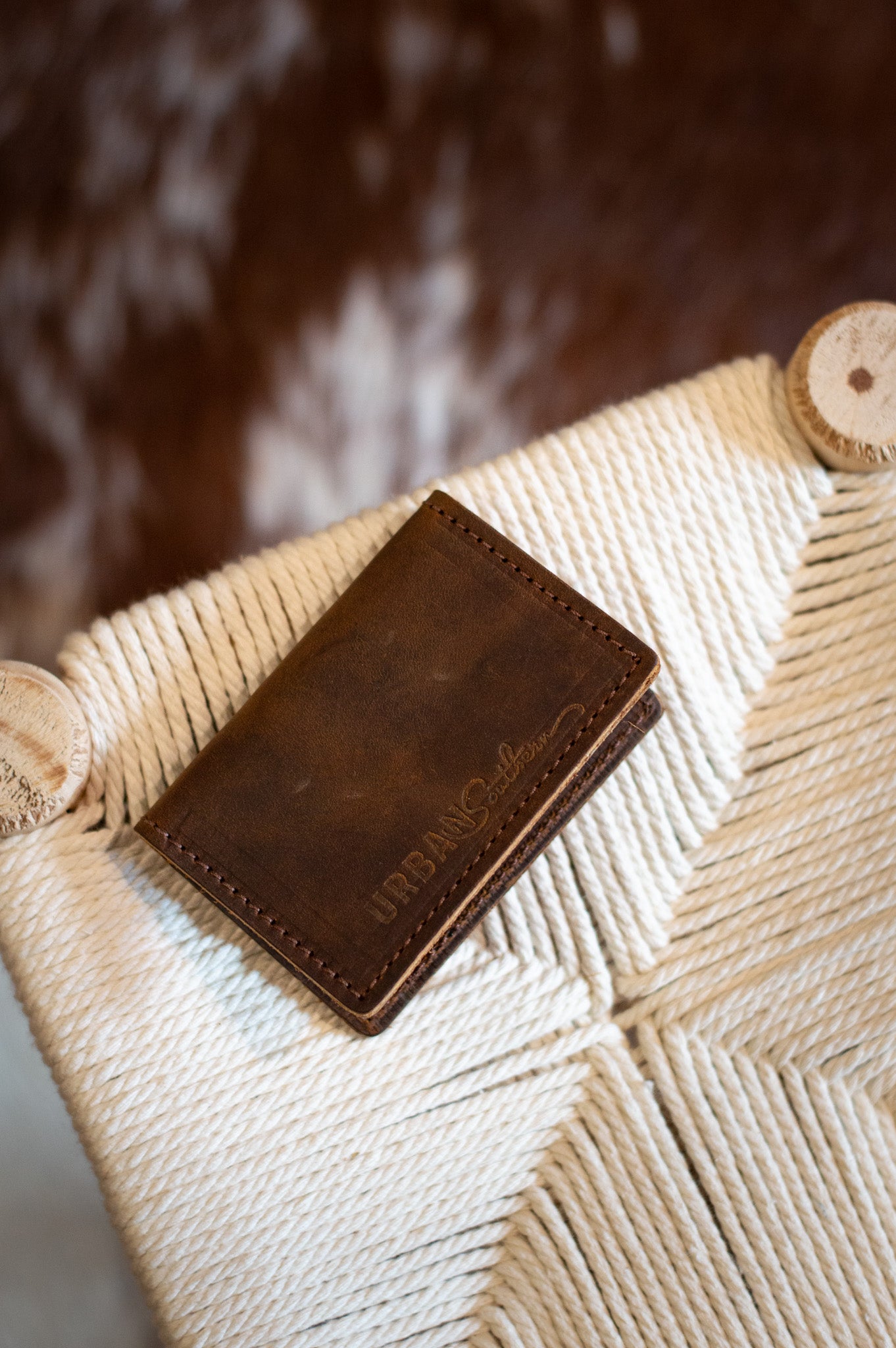 Rustic leather wallet displaying "Urban Southern" sits on a woven rope chair.

