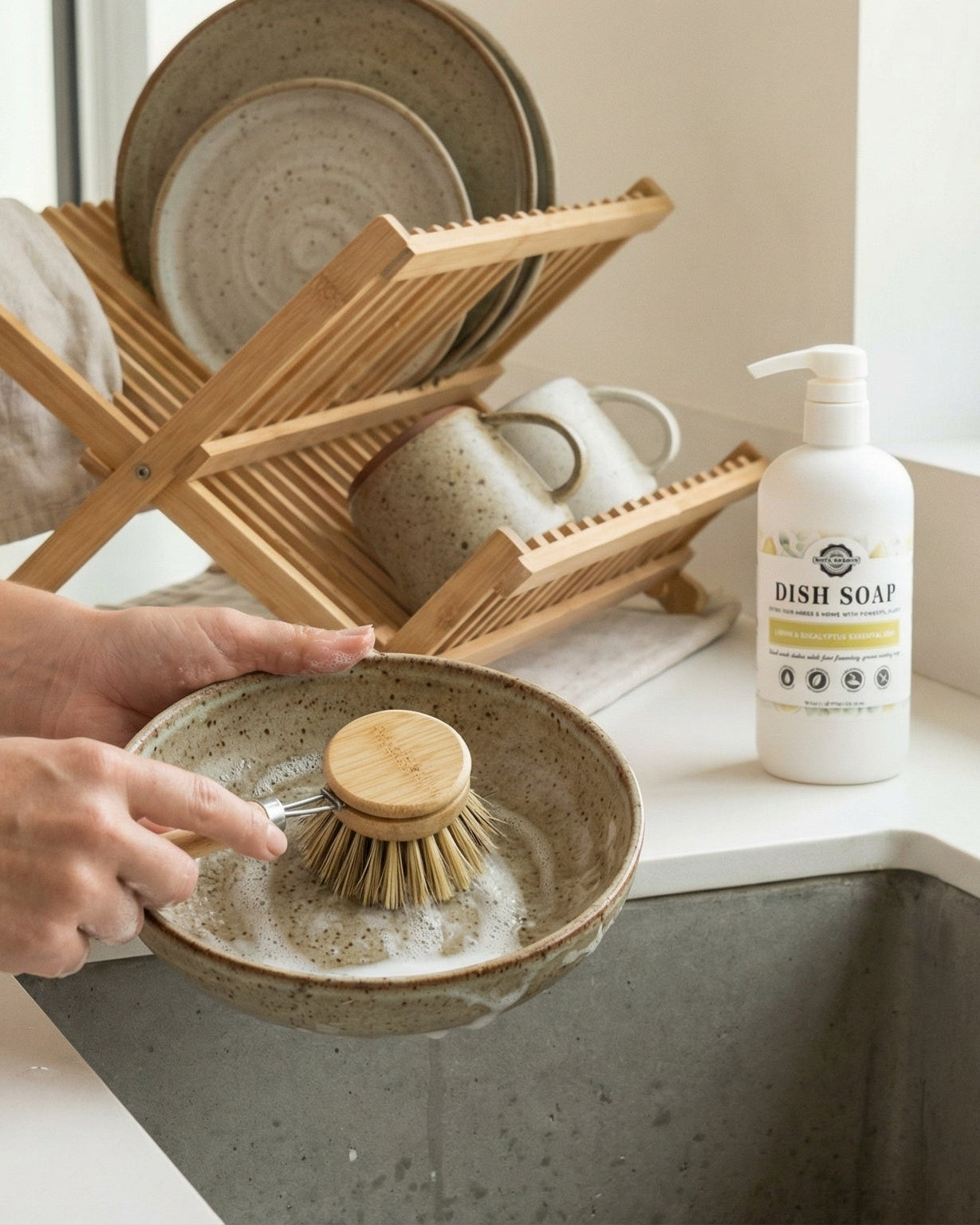 Person cleaning a ceramic dish with a wooden scrubber, next to a dish soap bottle on a kitchen counter.