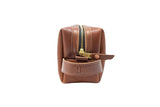 A brown leather Dopp kit displays a gold zipper and embossed "US" logo.
