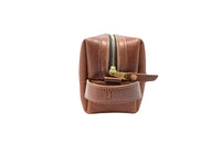 A brown leather Dopp kit displays a gold zipper and embossed "US" logo.
