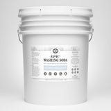 A large white bucket displays the label for Rustic Strength Epic Washing Soda, highlighting its unscented, hypoallergenic, and powerful stain-fighting qualities.
