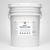 A large white bucket displays the label for Rustic Strength Epic Washing Soda, highlighting its unscented, hypoallergenic, and powerful stain-fighting qualities.
