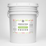 Examine a large white bucket filled with Rustic Strength Epsom Salt Soak, featuring bergamot and grapefruit essential oils for natural skin moisturizing.
