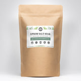 A kraft bag displays Rustic Strength Epsom Salt Soak with mint and eucalyptus essential oils, highlighting natural skin moisturizing benefits and biodegradable ingredients.