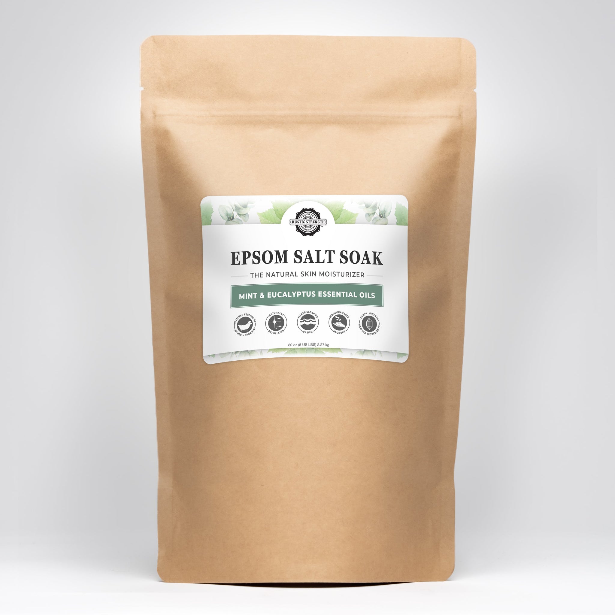 A brown paper bag displays a label promoting Rustic Strength Epsom Salt Soak with mint and eucalyptus essential oils, highlighting its natural skin moisturizing and muscle-relaxing properties.