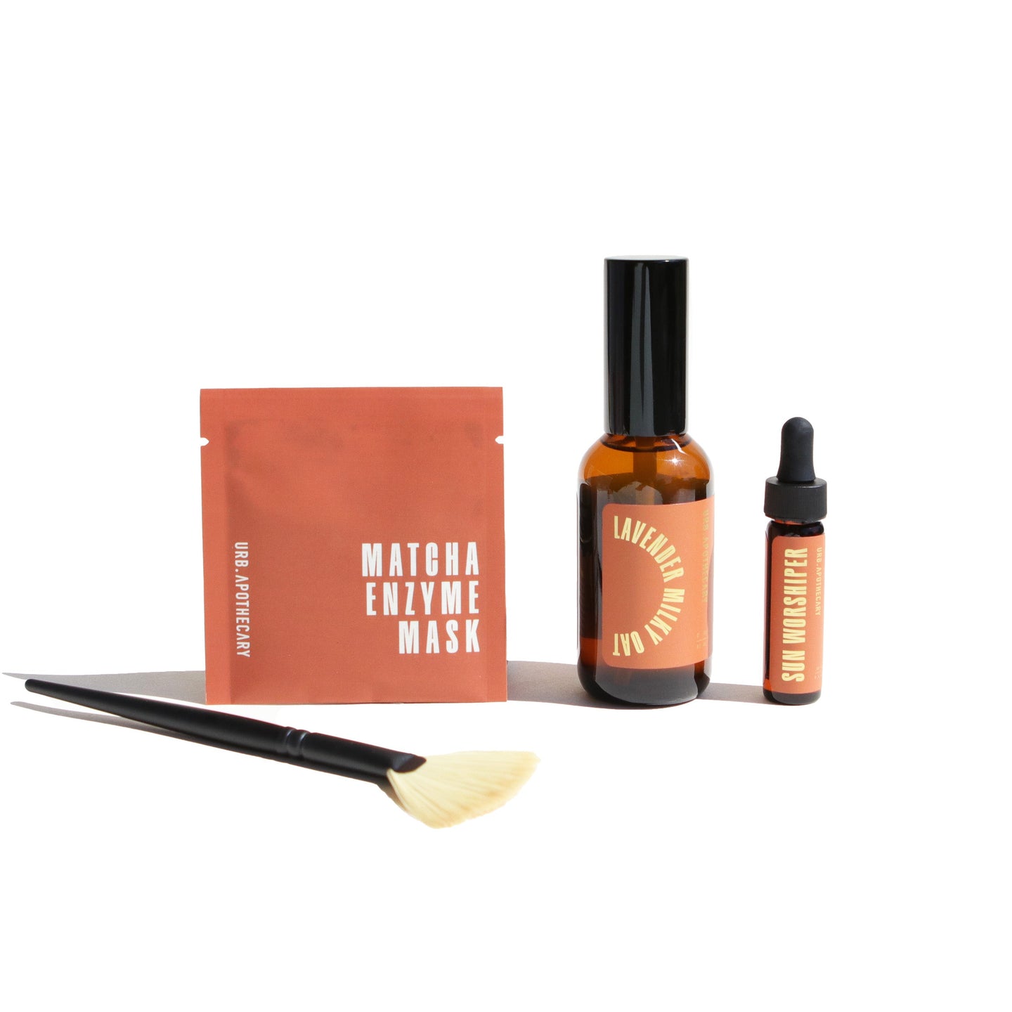 Urb Apothecary displays their skincare line including a Matcha Enzyme Mask, Lavender Milky Oat Serum, and Sun Worshiper oil with an applicator brush.
