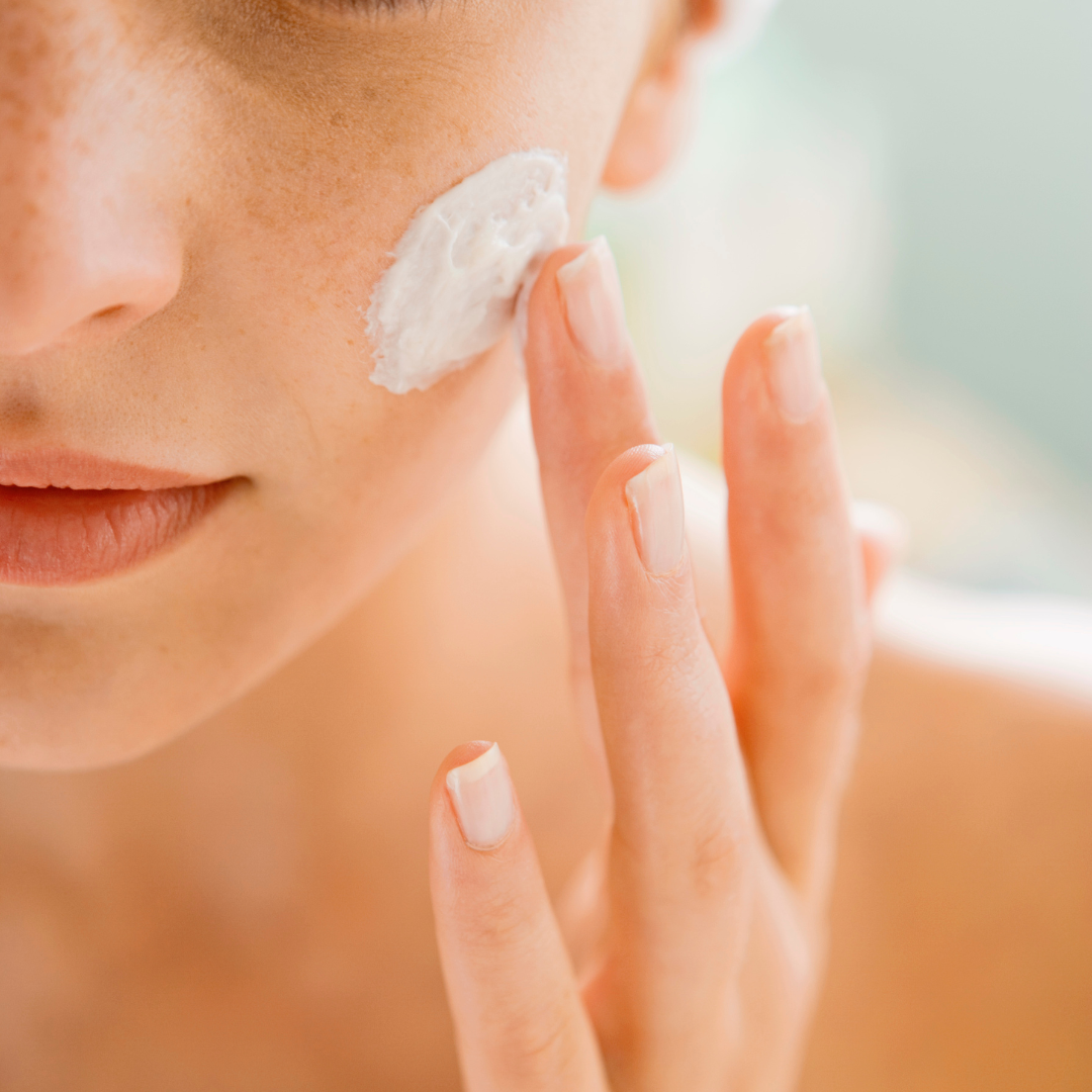 A woman applies moisturizing cream to her face for skincare.
