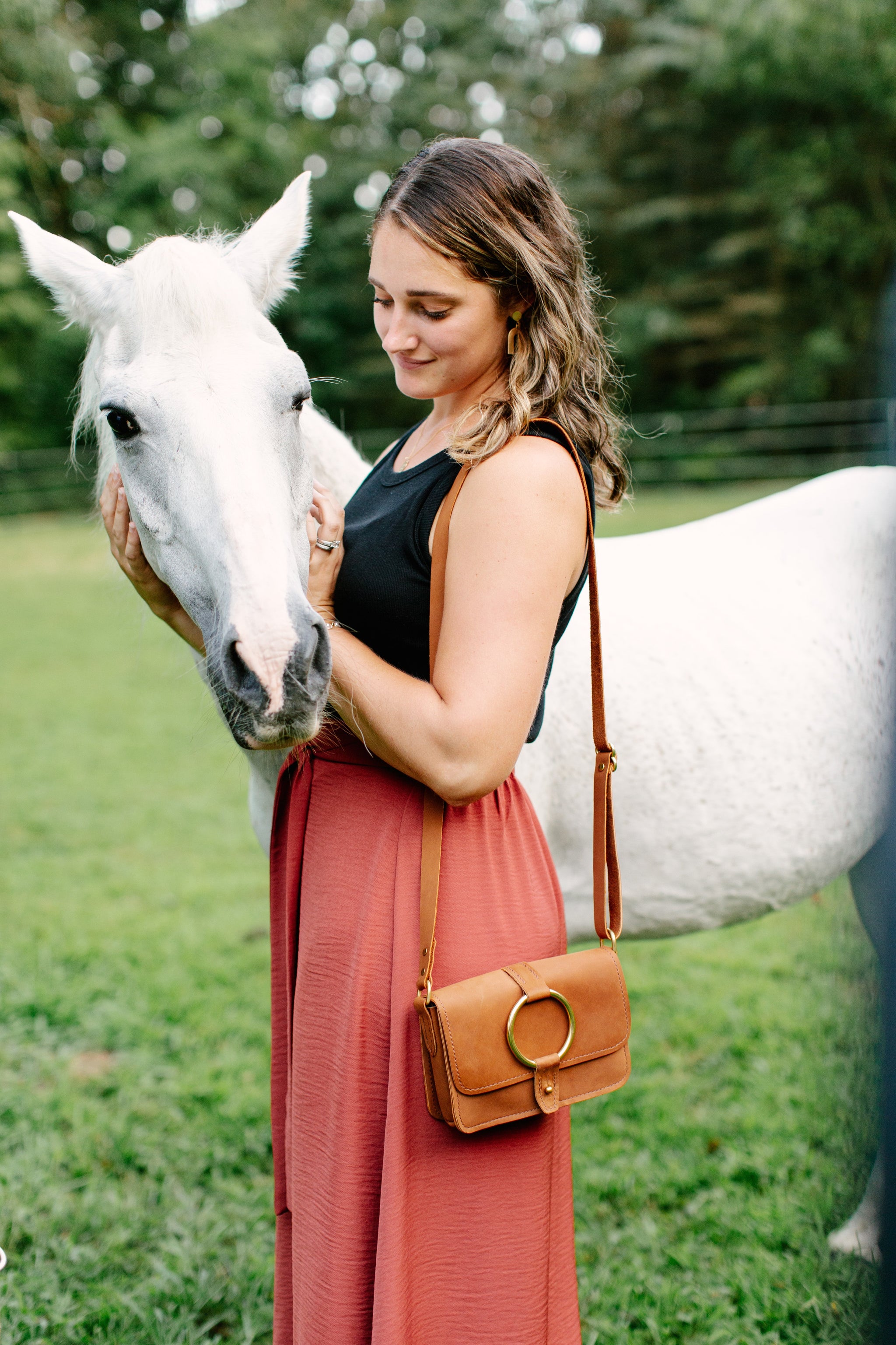 A woman gently pets a beautiful white horse in a grassy field.
