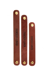 Three brown leather cable straps, each with a brass snap, display the phrase "FIERCELY LOVED".
