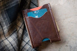 Close-up shows an Urban Southern leather card holder wallet with credit cards and cash against a plaid shirt.
