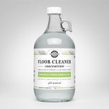 View showcases a glass jug of Rustic Strength floor cleaner concentrate featuring bergamot and cypress essential oils.
