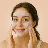 A woman applies a foamy face cleanser to her skin for her skincare routine.
