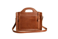 A brown leather satchel handbag featuring a top handle and shoulder strap sits against a white background.
