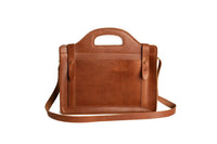 A brown leather satchel handbag featuring a top handle and shoulder strap sits against a white background.
