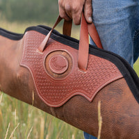 Brown leather gun case with handle held by a person in a field