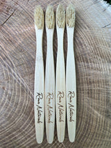 Four "Rowe Naturals" bamboo toothbrushes sit vertically on a textured wooden surface.
