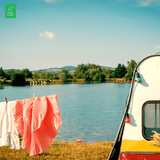 Clothes dry on a line strung between a vintage camper and trees by a serene lake on a camping trip.
