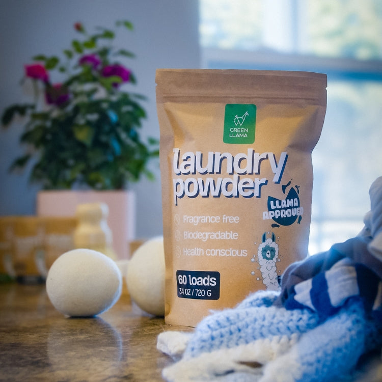 Green Llama laundry powder and wool dryer balls sit on a countertop near folded laundry.
