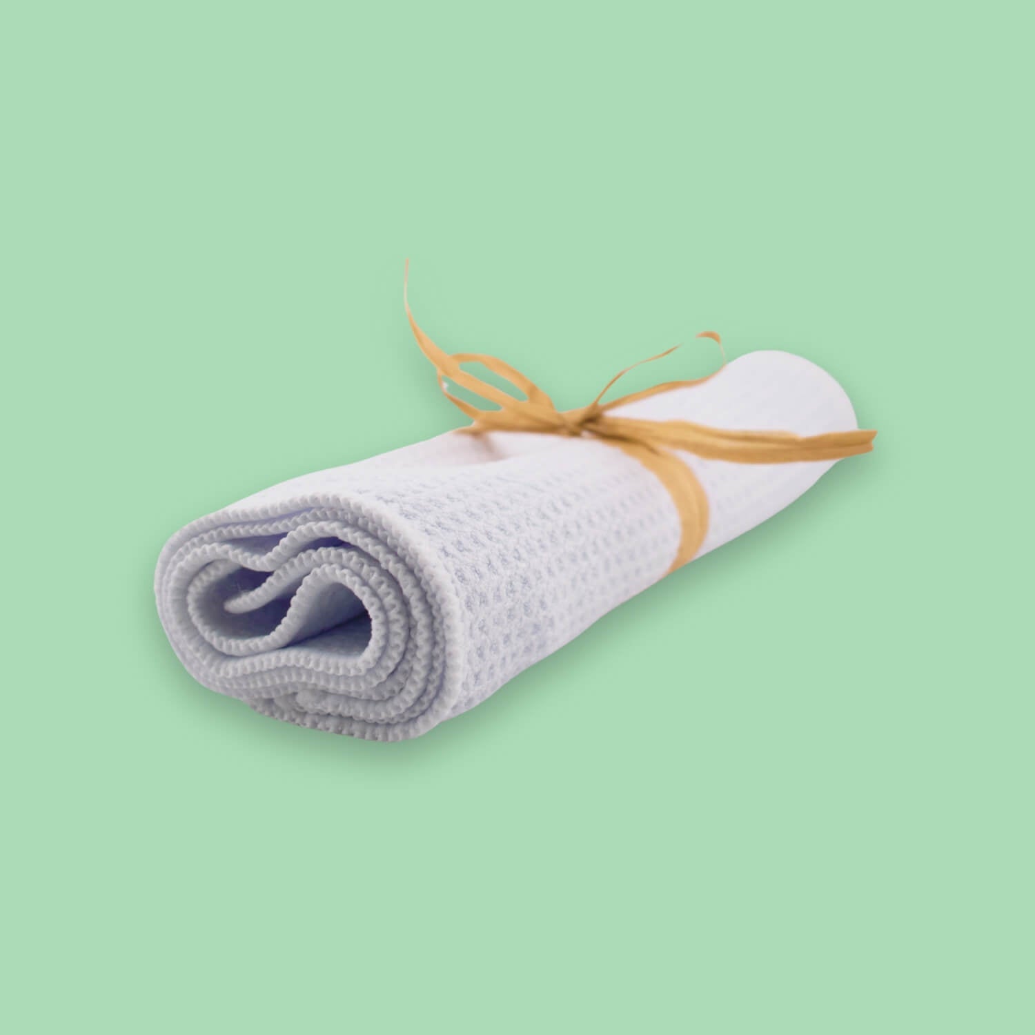 A rolled white waffle weave towel sits tied with a tan raffia ribbon.
