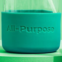 Close-up shows a reusable glass bottle with a teal silicone sleeve labeled "All-Purpose" and a white straw.
