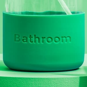 Close-up shows a green bathroom accessory with the word "Bathroom" embossed, featuring a white straw.
