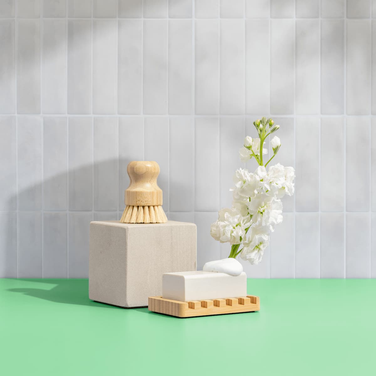 A dish brush sits on a block next to a bar of soap with a flower on a bright green counter.
