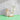 A dish brush sits on a block next to a bar of soap with a flower on a bright green counter.
