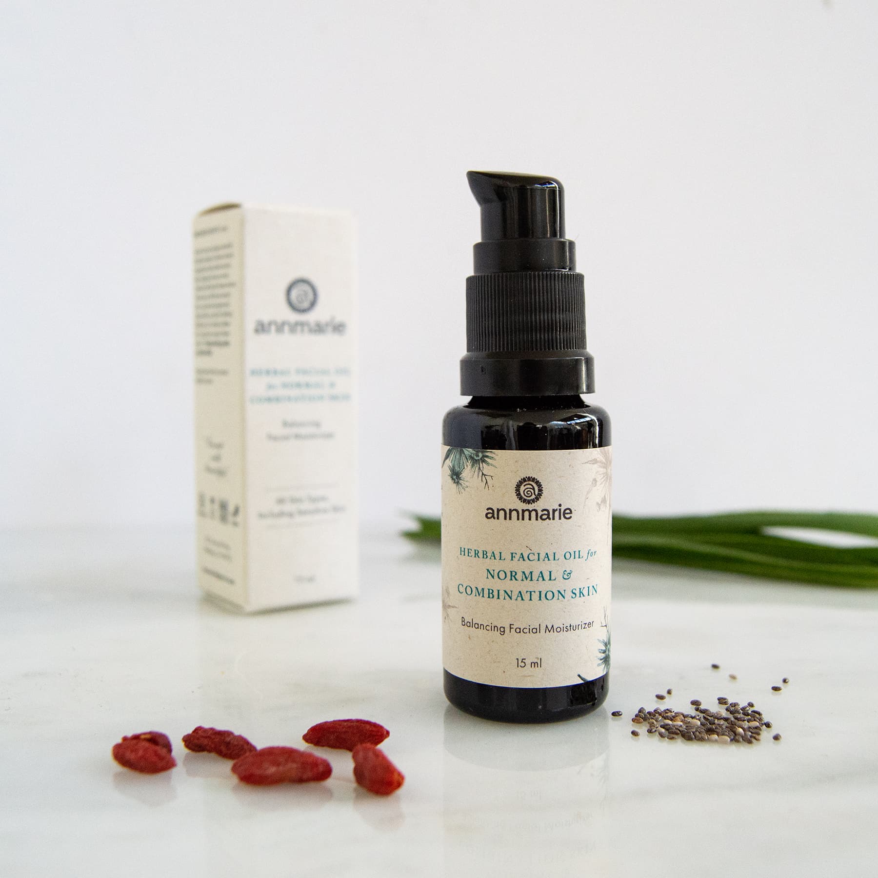 Annmarie herbal facial oil for normal and combination skin sits beside its packaging and goji berries on a marble surface.
