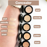 Woman's arm swatches and showcases various shades of cream concealer makeup in compacts for skin tone matching.
