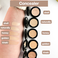 Woman's arm swatches and showcases various shades of cream concealer makeup in compacts for skin tone matching.

