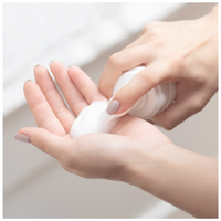 A woman dispenses foaming cleanser into her palm for skincare.

