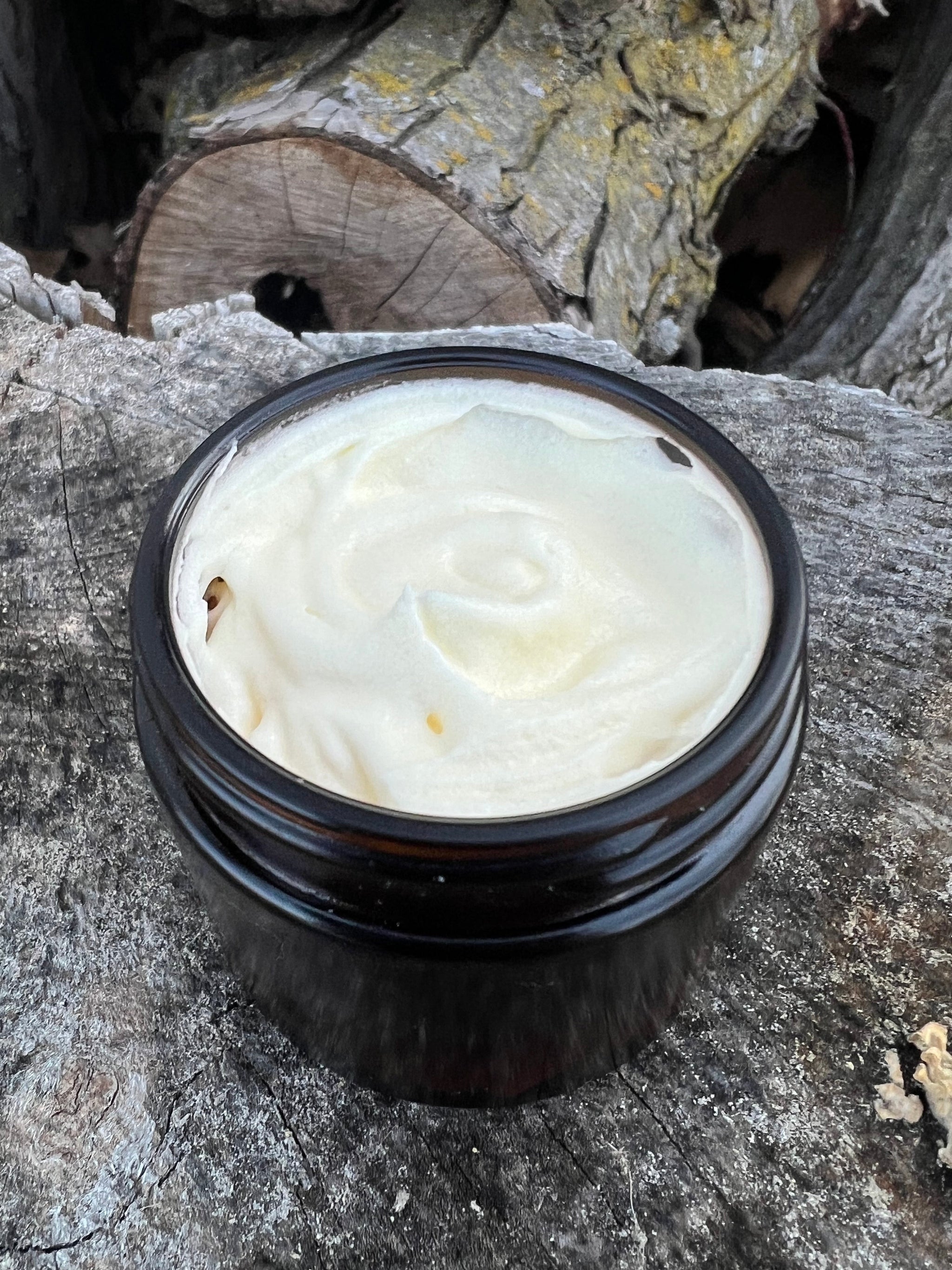 Close-up shows a jar of homemade whipped shea butter cream on a weathered wood surface.
