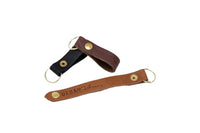Three leather keychains, including black, brown, and tan "Urban Southern" branded styles, feature brass hardware and lie on a white background.